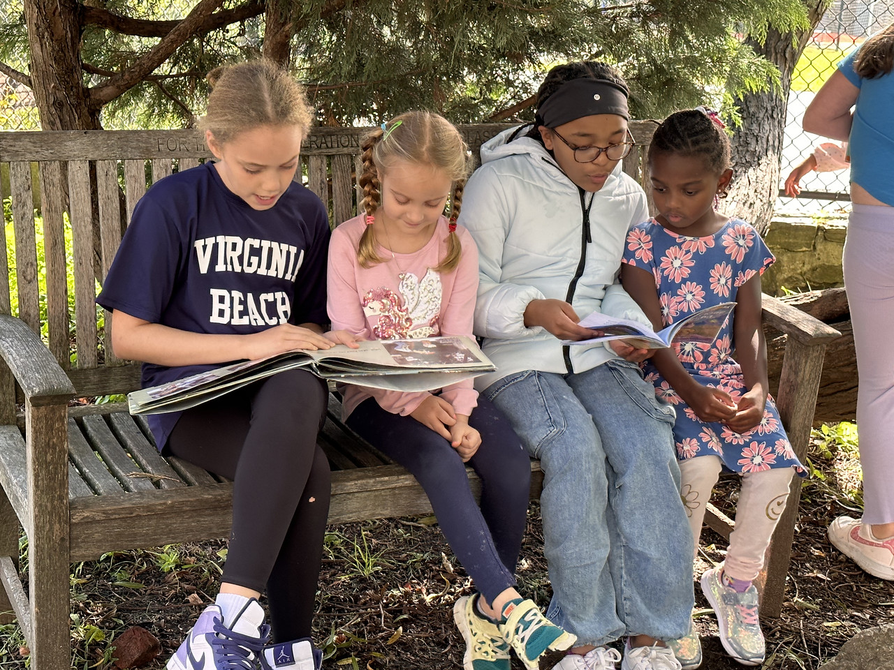 Group of four Fieldston Lower students read together on a bench outside.