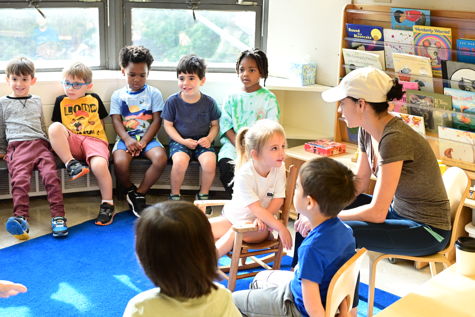 Fieldston Lower Pre-K students listen to teacher in a circle in classroom. One student sits in the middle.