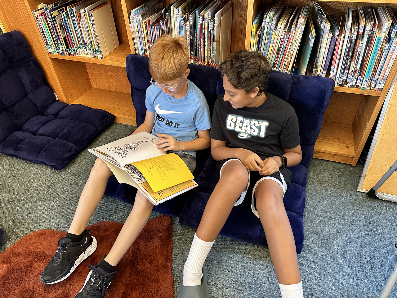 Two Fieldston Lower students sit on the floor in the library and read together.