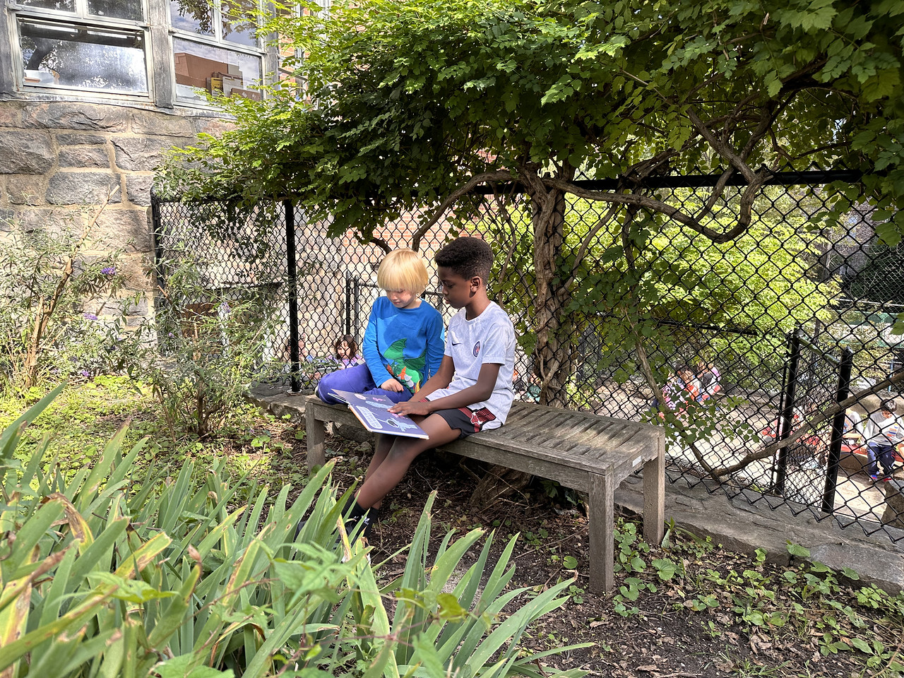 Two Fieldston Lower students read together on a bench outside.