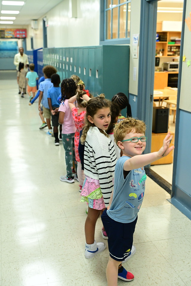 A Fieldston Lower Pre-K line-leader smiles and raises his hand.