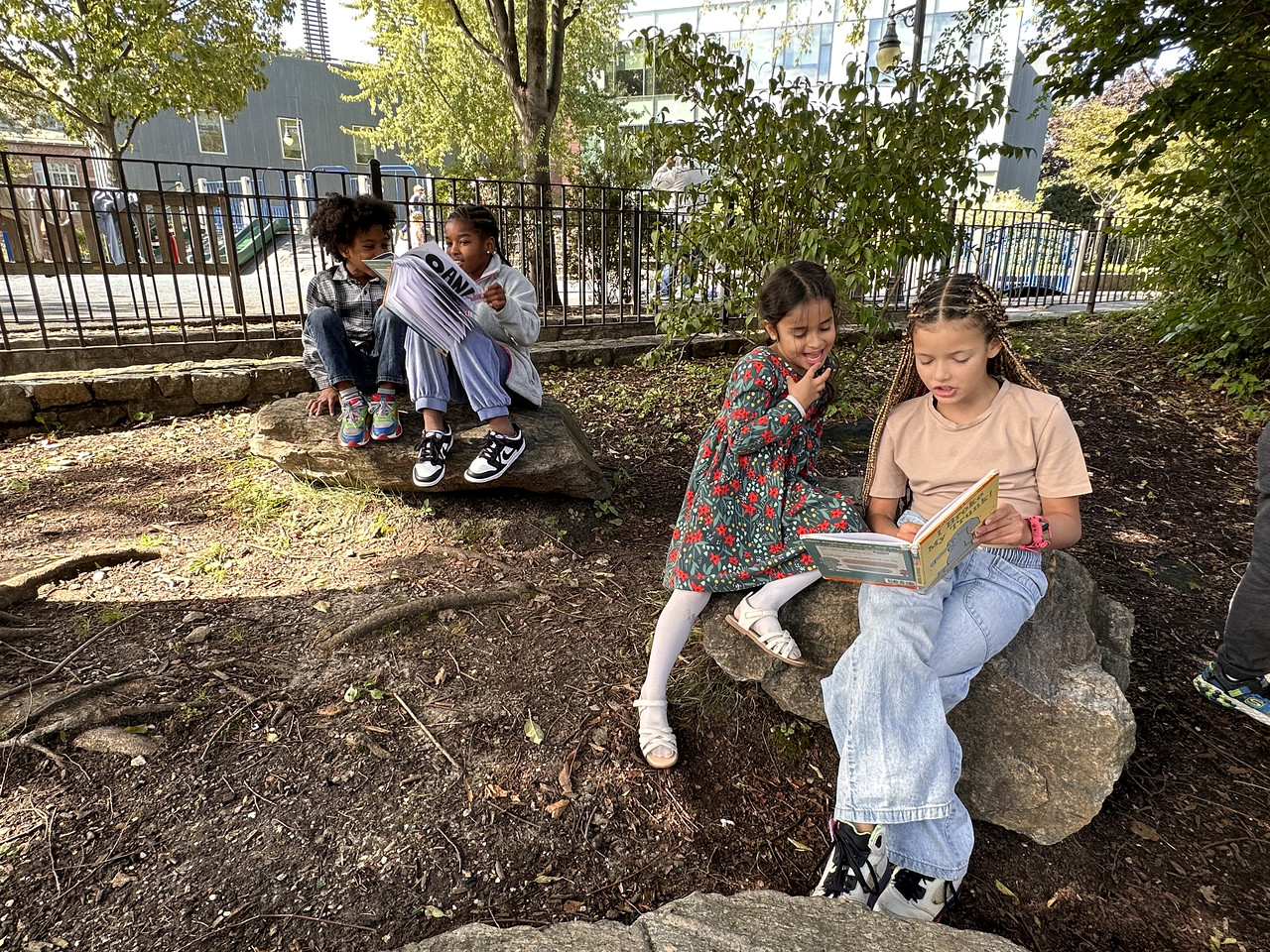 Two Fieldston Lower students read together while sitting on a rock in the outdoor garden.