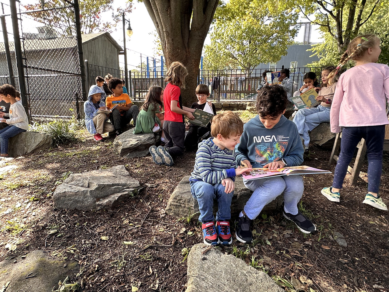 Two Fieldston Lower students read together while sitting on a rock in the Fieldston Lower garden.