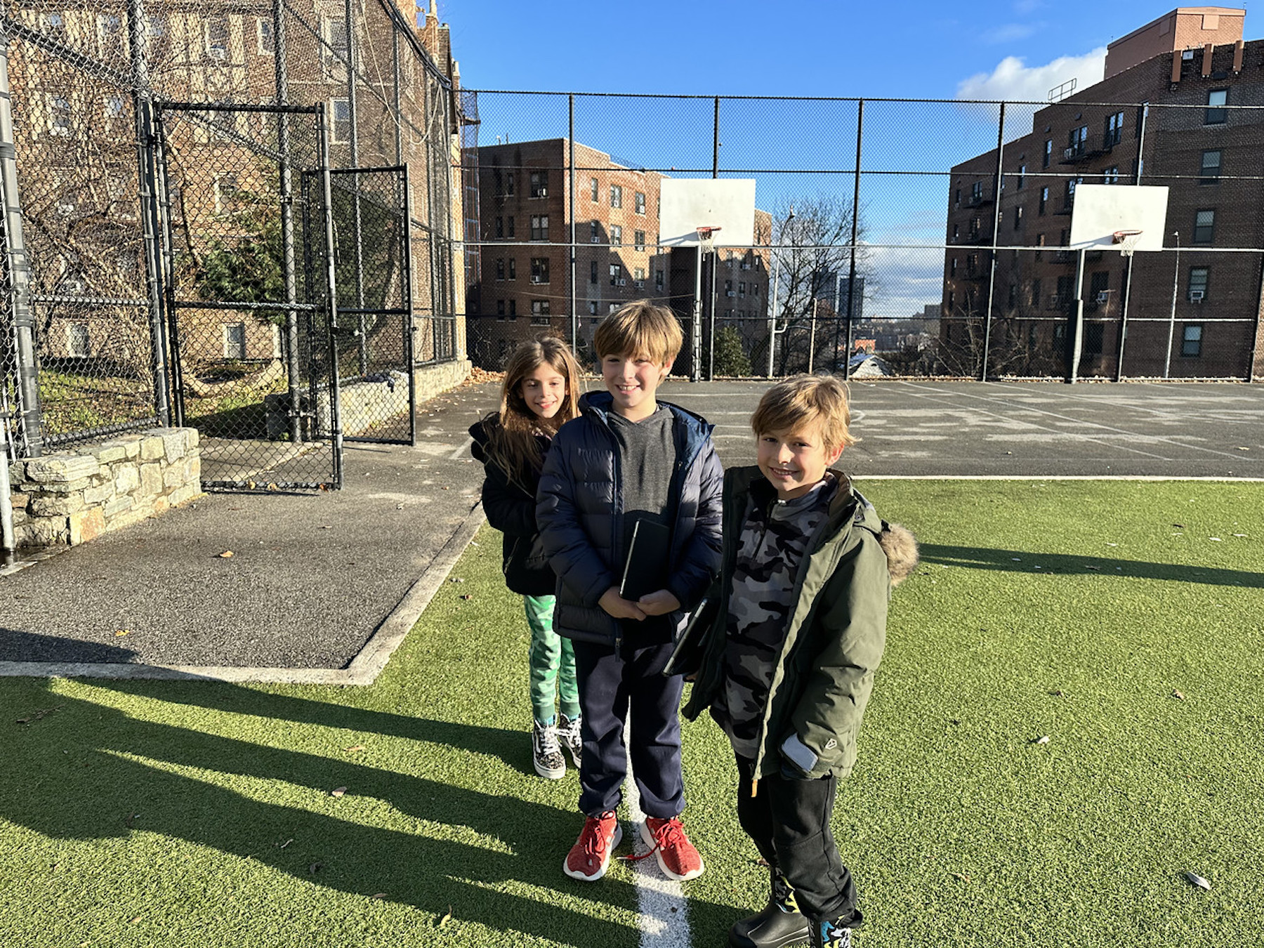 Three Fieldston Lower students pose and smile outdoors on the lower field.