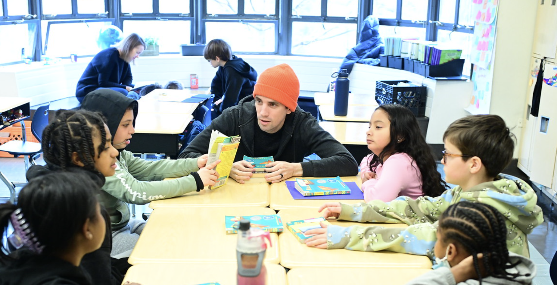 Fieldston Lower students gather around desks and listen to teacher as they discuss a text.