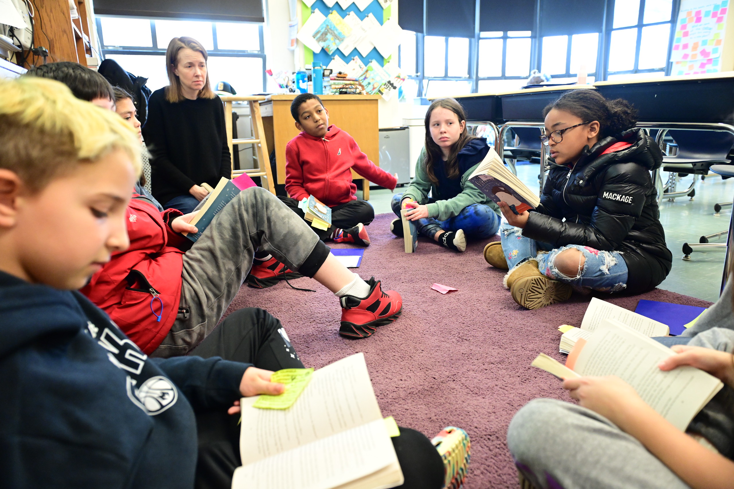 Fieldston Lower students sit on the carpet in a circle discussing a text during book club.