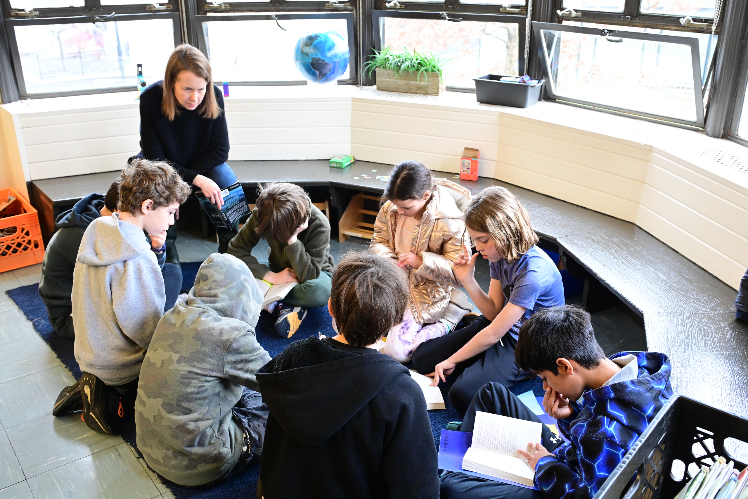 Fieldston Lower students gather in book club group on the carpet and listen to teacher as they discuss a text.