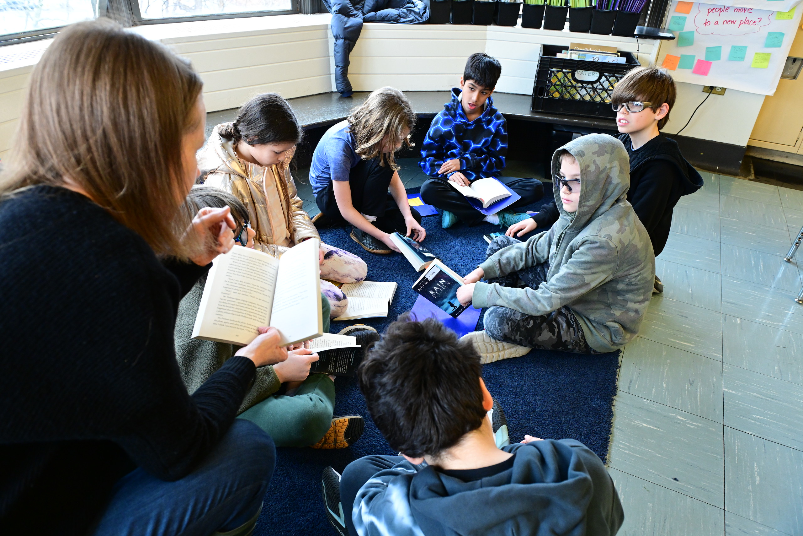 Over-the-shoulder shot of teacher reading to Fieldston Lower students sitting in a circle on the floor.