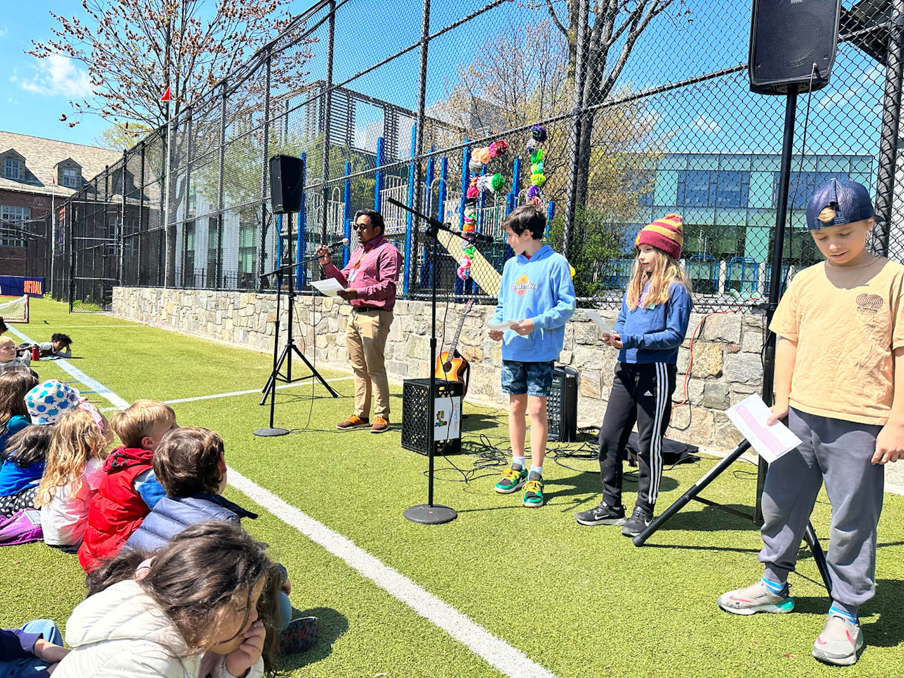 Fieldston Lower Assistant Principal Shawn Chisty speaks at Earth Day assembly on lower field. Other students stand nearby waiting to speak.