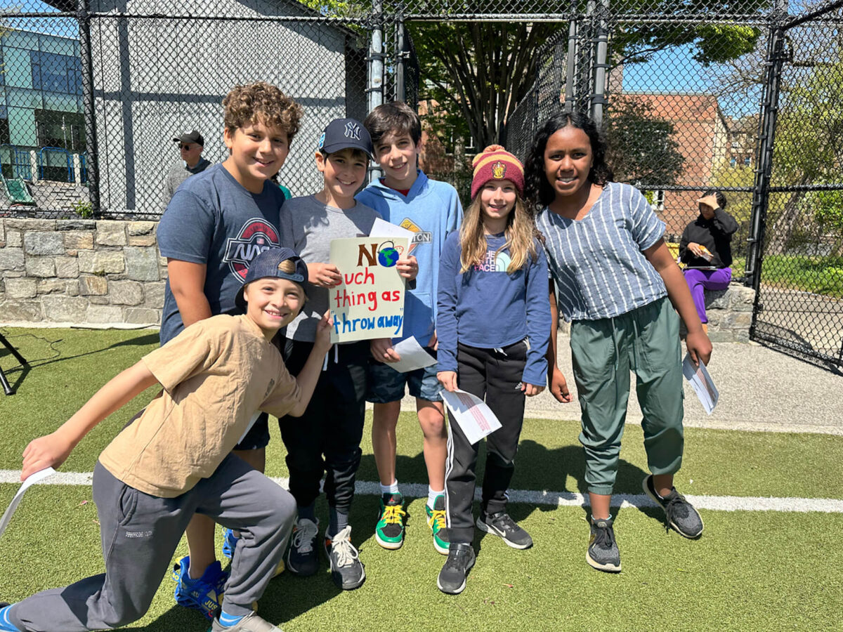 Group of 5th Grade Fieldston Lower students stand together smiling on the lower field and holding a sign that reads, "No such thing as throw away" at the Earth Day assembly.