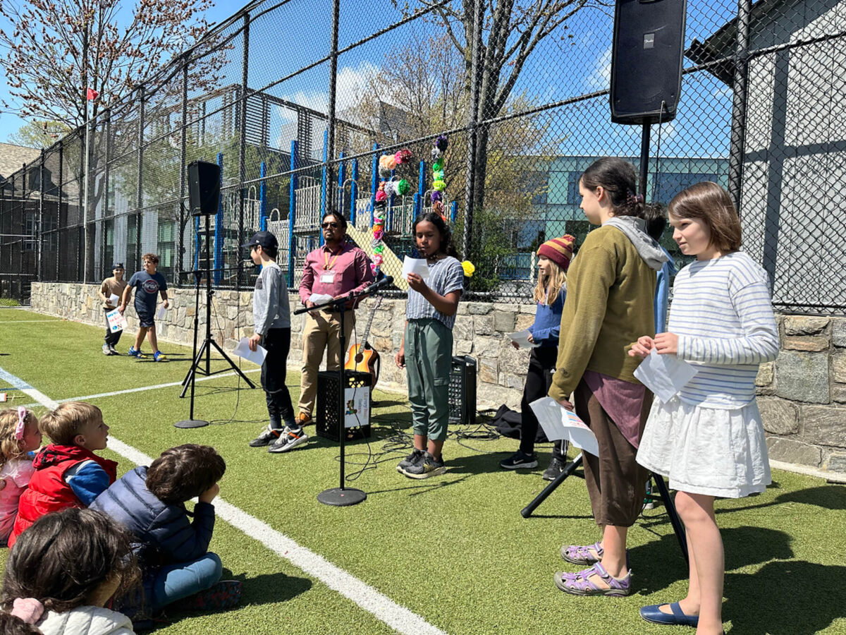 5th Grade Fieldston Lower student speaks into microphone at Earth Day assembly on the lower field as her classmates look on.