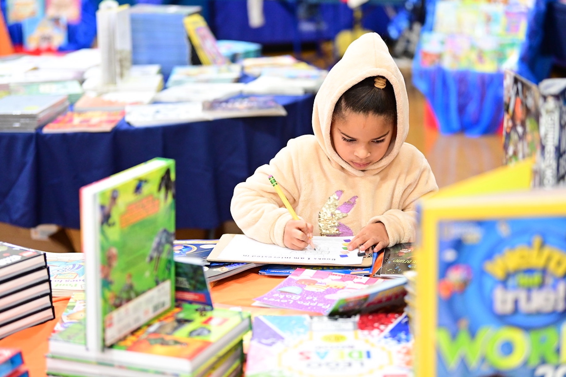 Fieldston Lower students writes down the name of a book using a pencil at the book fair.