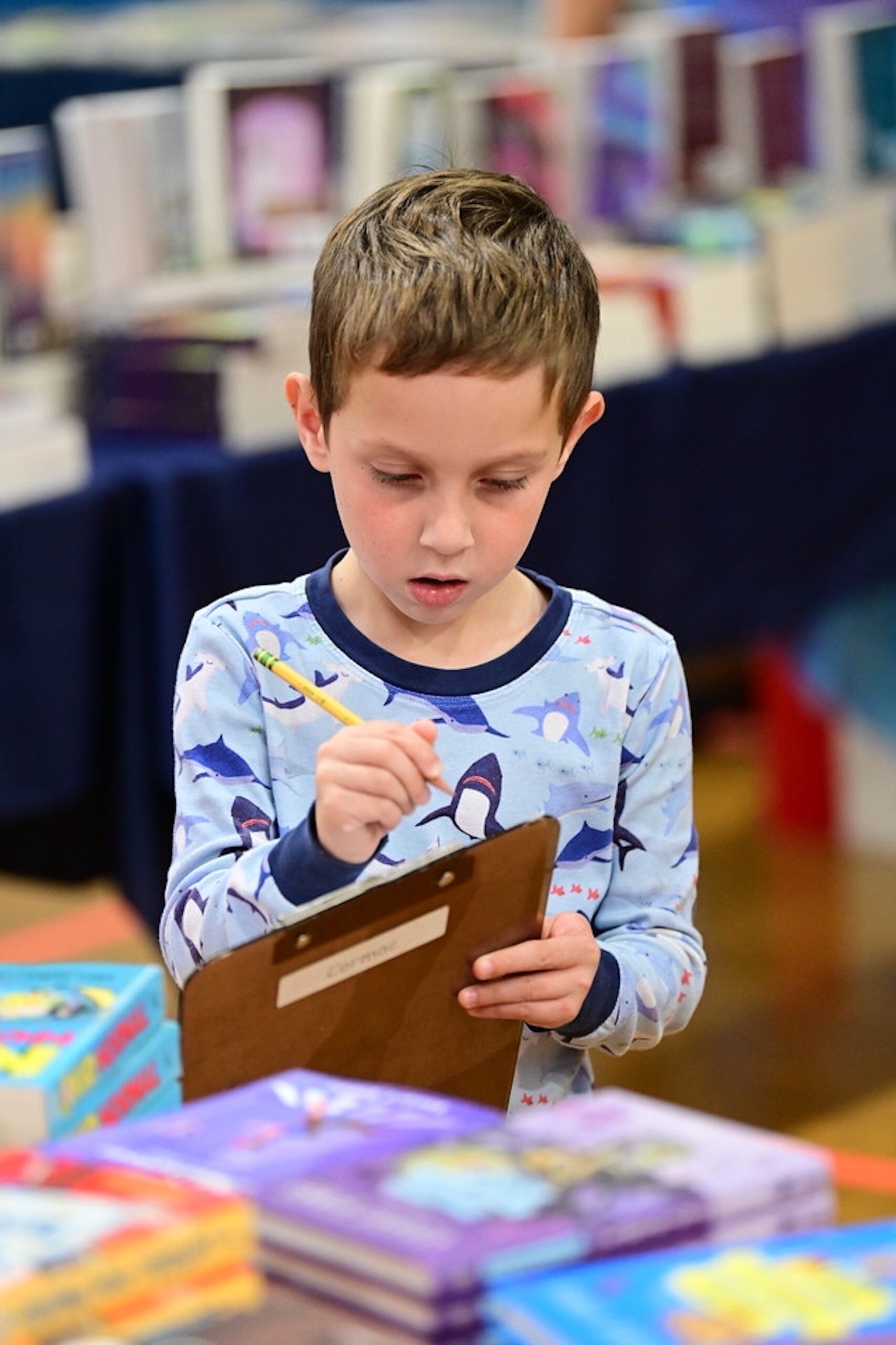 Fieldston Lower students writes down the name of a book using a pencil at the book fair.