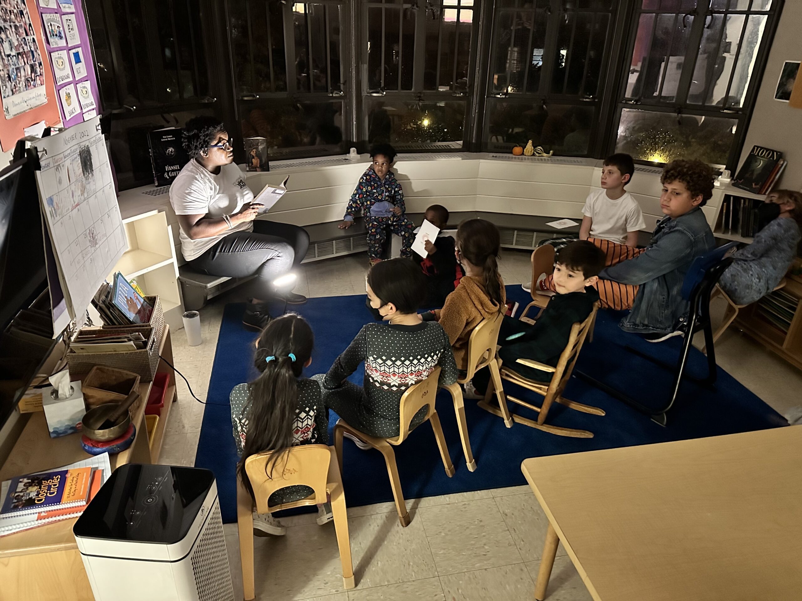 Fieldston Lower Assistant Principal Naomi Randolph reads to a room full of students in the dark; they sit on the floor in pajamas and listen along.