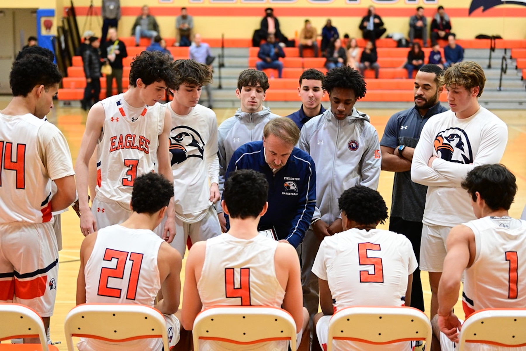 Fieldston Upper boys varsity basketball players huddle around the bench and listen as their coach draws out a play.