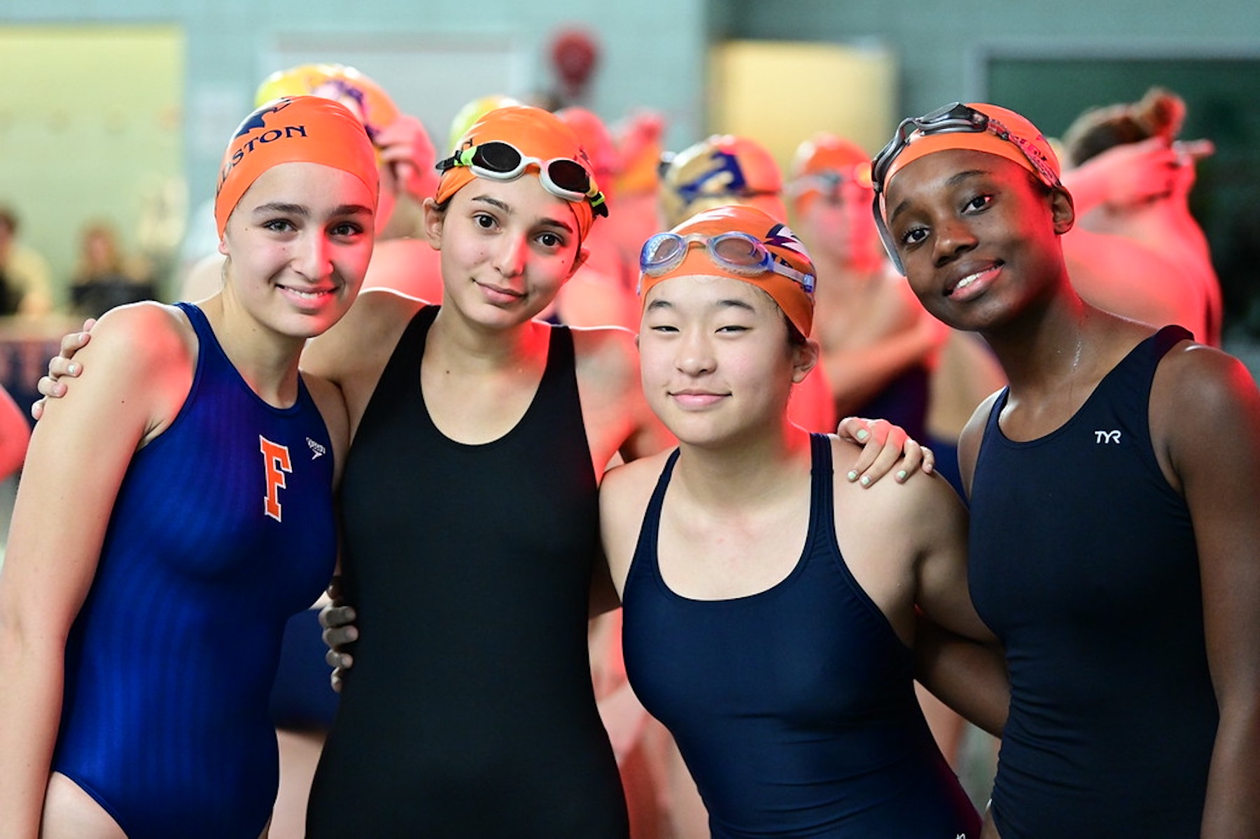 Four Fieldston Upper swimmers pose and smile while looking at the camera.
