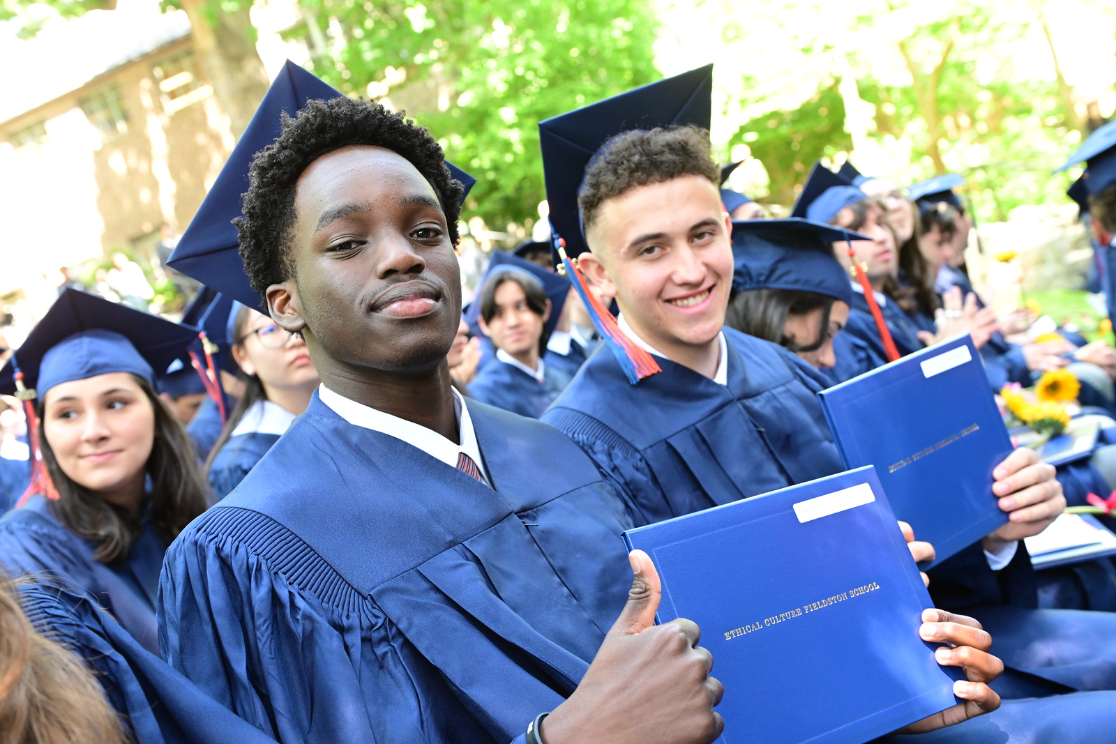 Fieldston Upper students pose and give a thumbs up with their diplomas at Commencement.