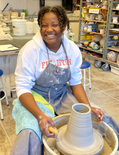 Fieldston Upper student poses and smiles while working on ceramics project in art studio. 