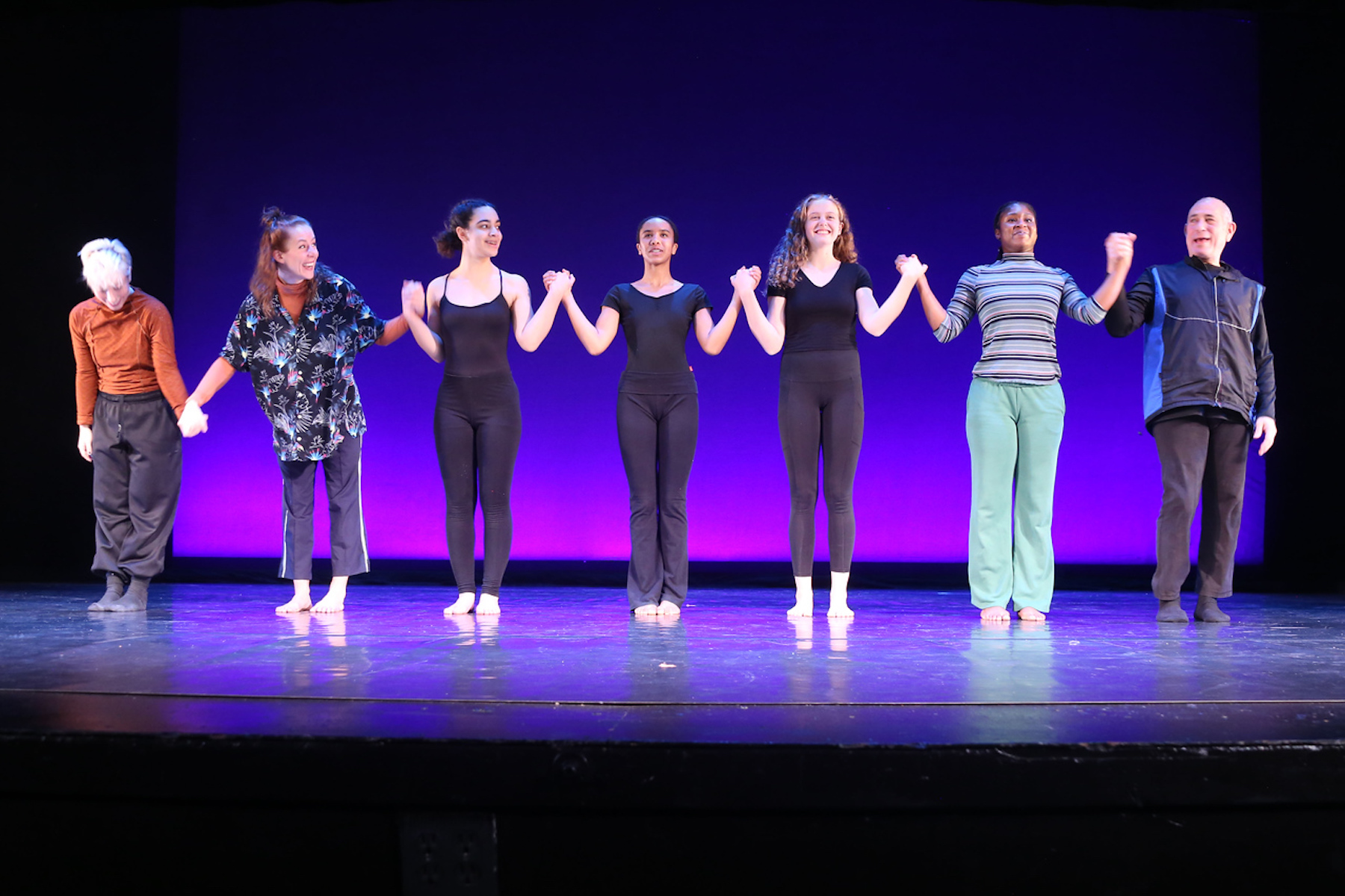 Dancers hold hands in a line and prepare to take a bow on stage.