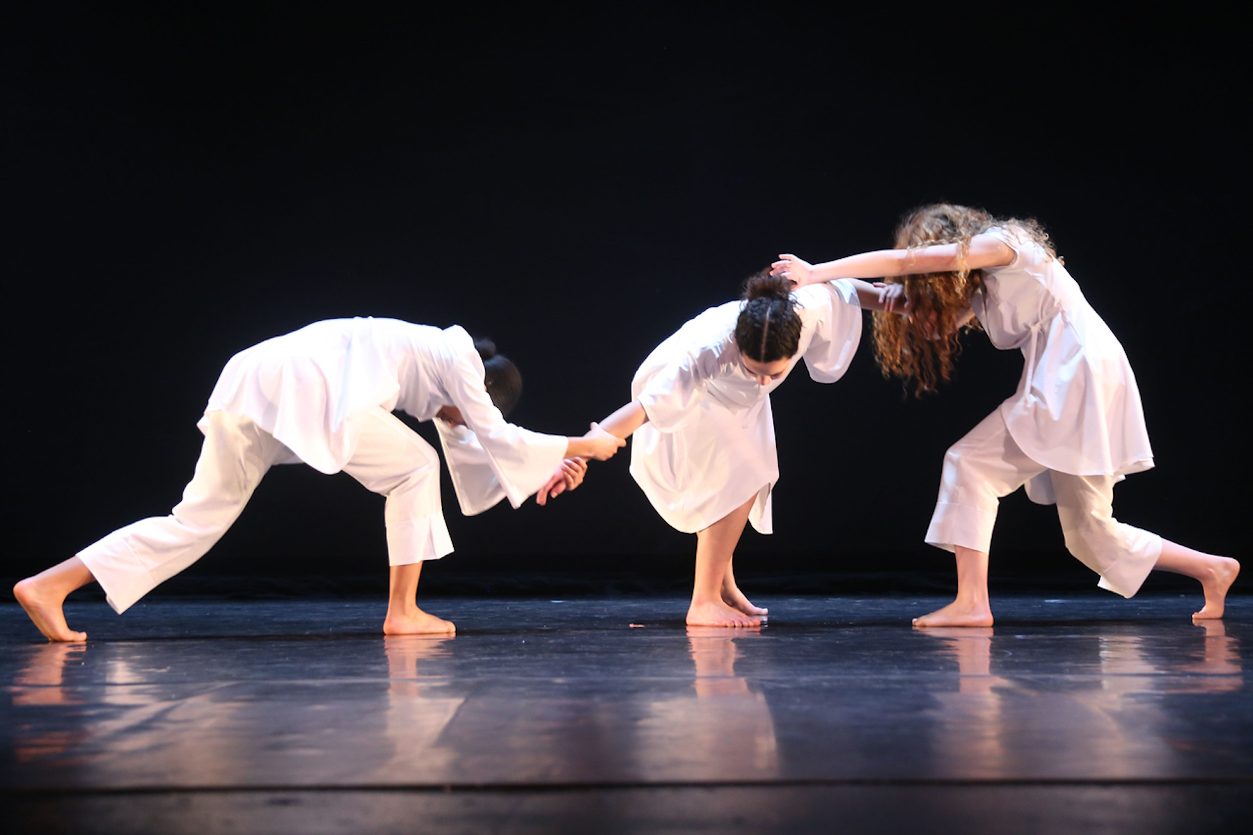 Three Fieldston Upper dancers perform on stage, wearing all white.