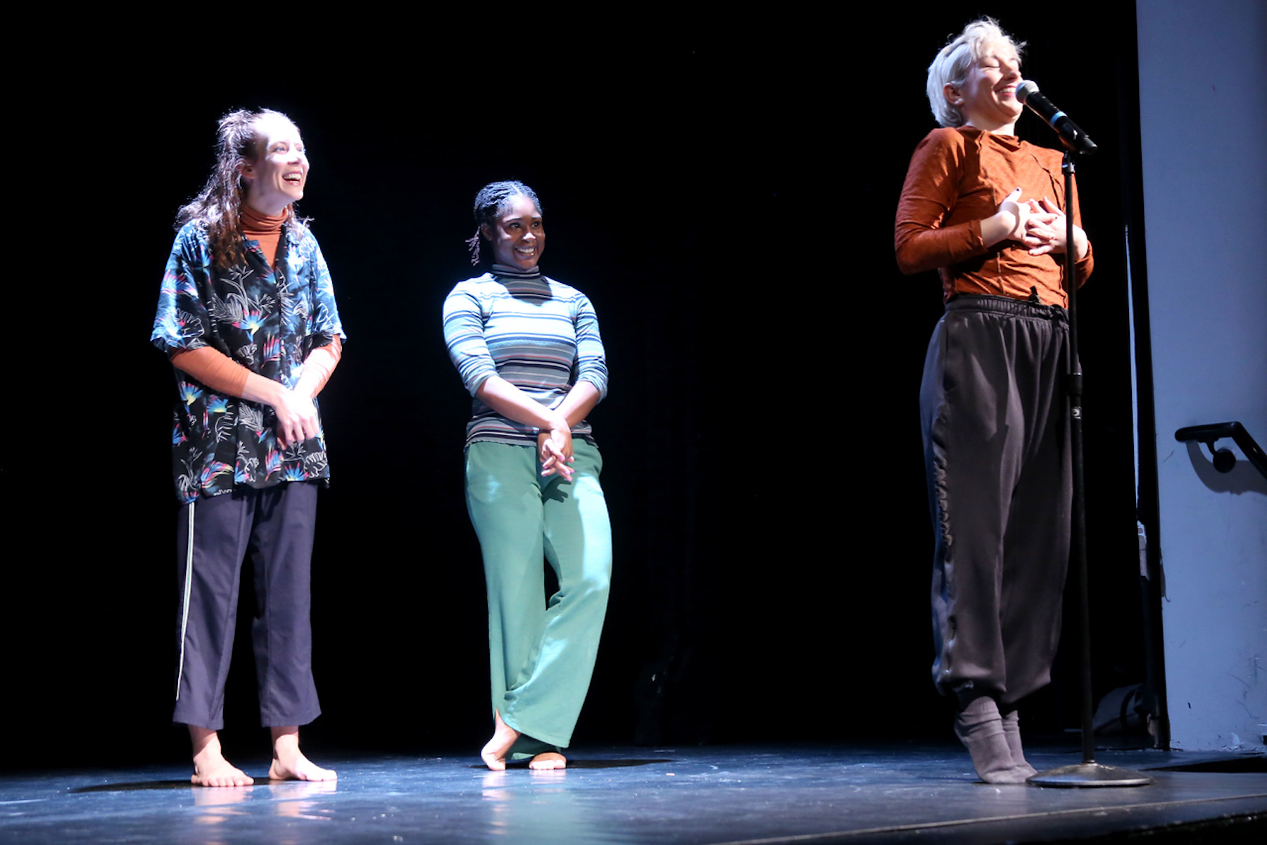 David Dorfman dancer introduces piece at the microphone, while two others smile in the background.