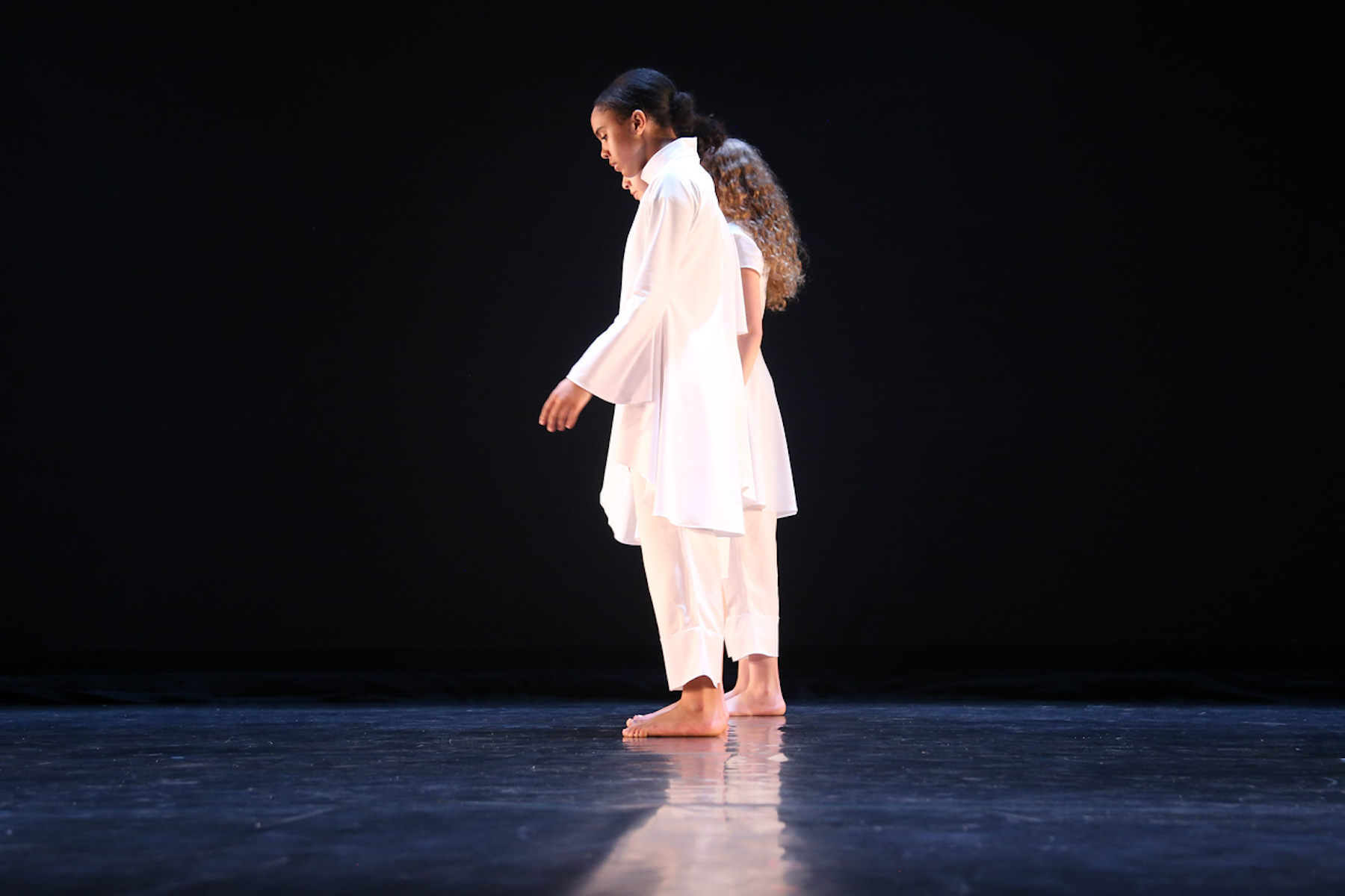 Fieldston Upper dancers prepare to perform on stage, wearing all white.