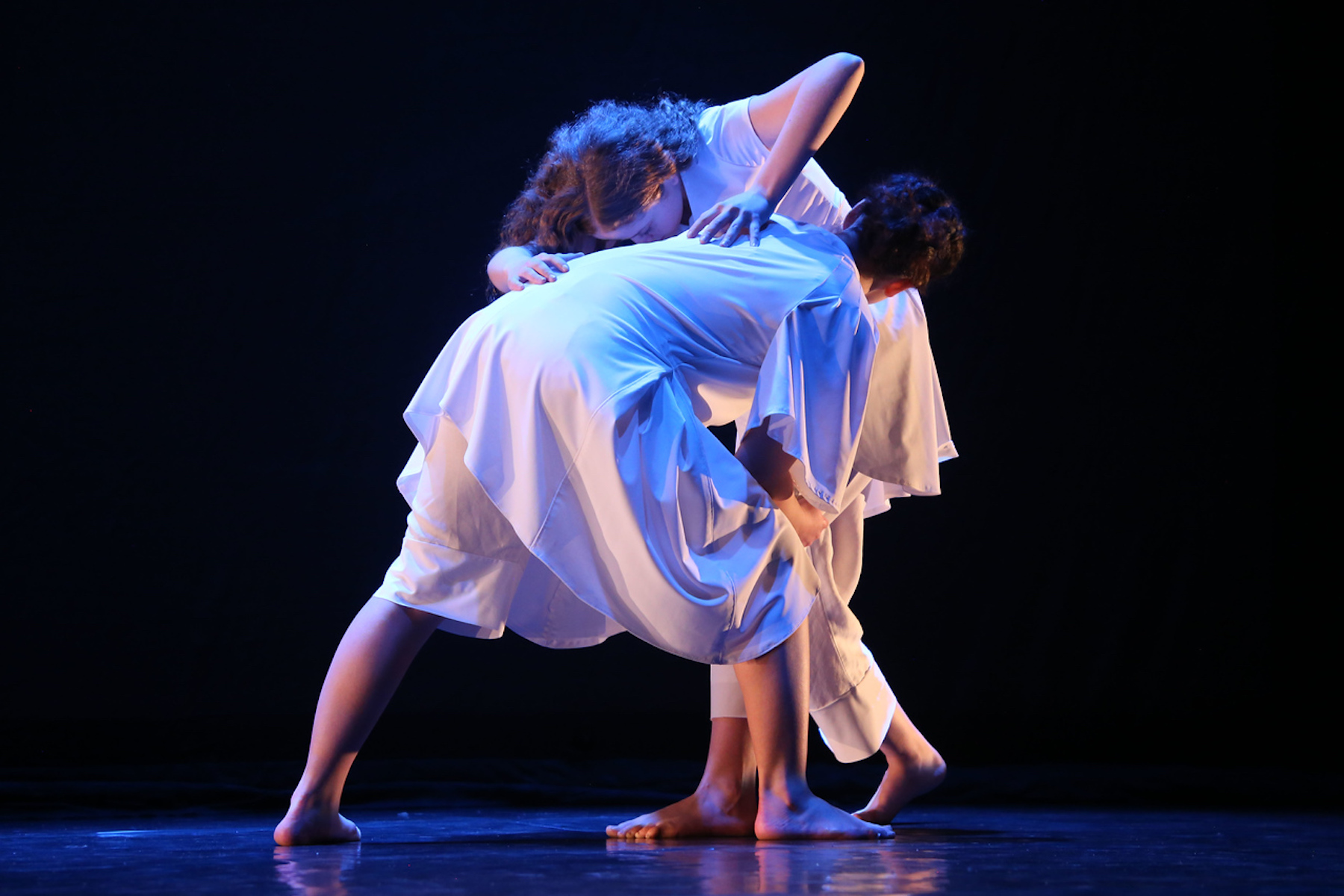 Fieldston Upper dancers perform routine on stage, wearing all white, the background is dark.