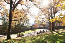 A wide view of the Fieldston quad with fall foliage and students in the distance sitting on benches.