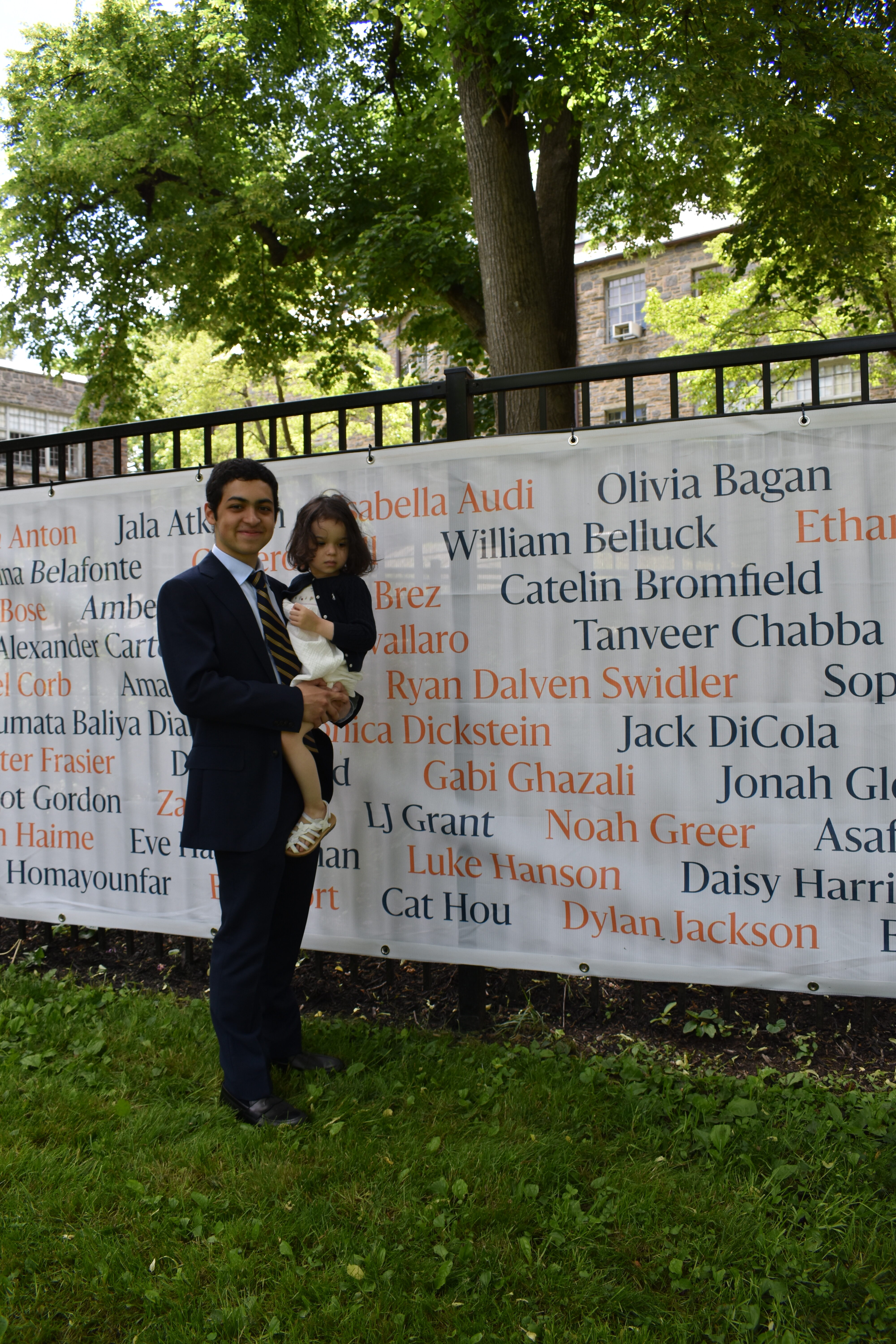 Gabi Ghazali poses in front of his name on a banner showing the names of ECFS's graduating class.