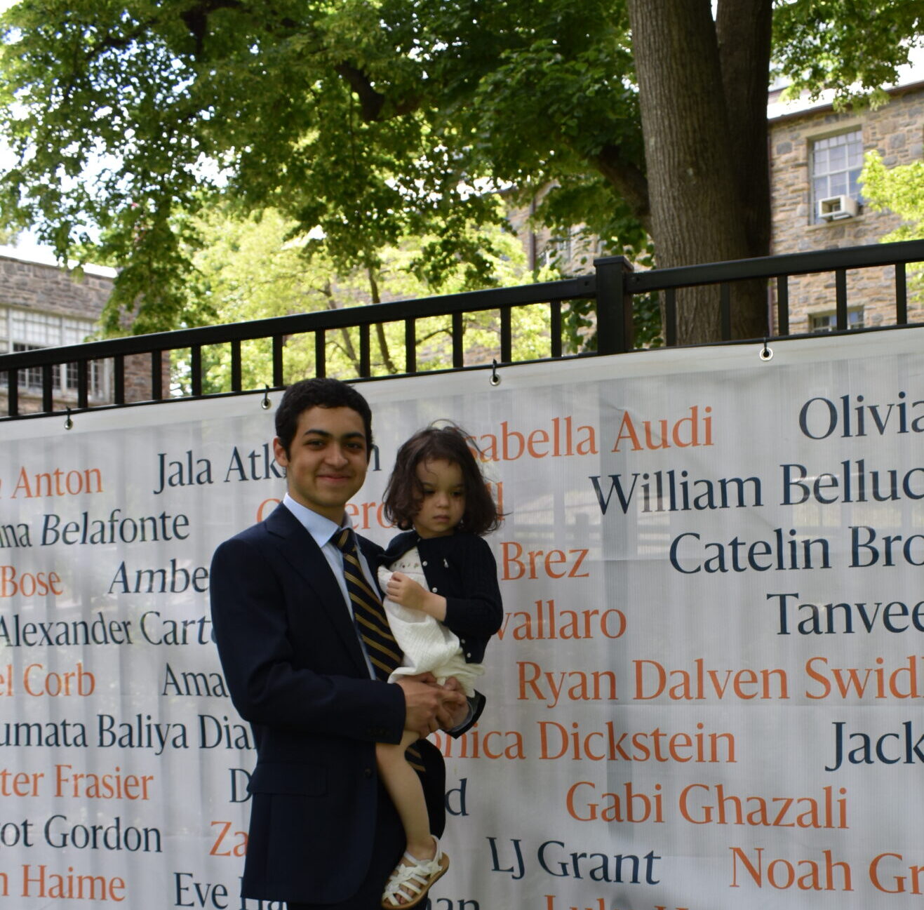 Gabi Ghazali poses in front of his name on a banner showing the names of ECFS's graduating class.