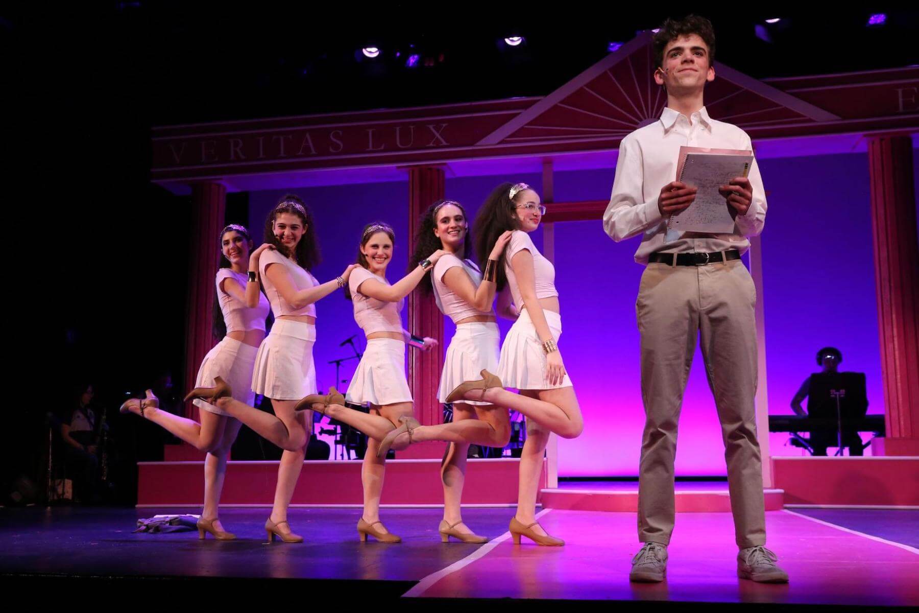 Four Ethical Culture Fieldston Upper School students pose onstage while one student stands in front of them in Legally Blonde.