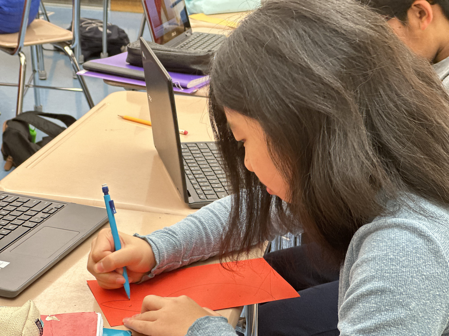 Student uses pencil to trace an outline on red paper.