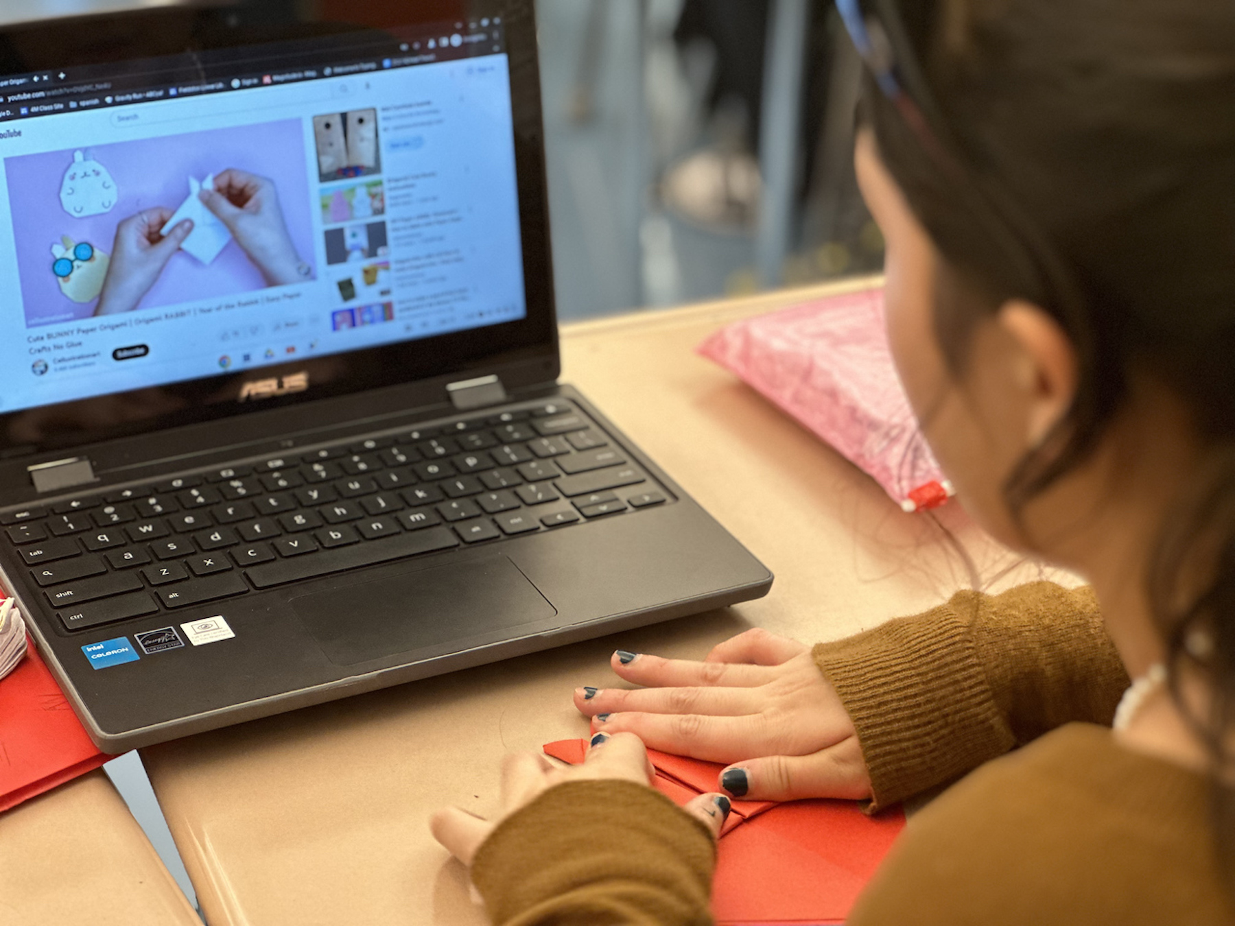 Student looks at computer tutorial while folding a rabbit origami.