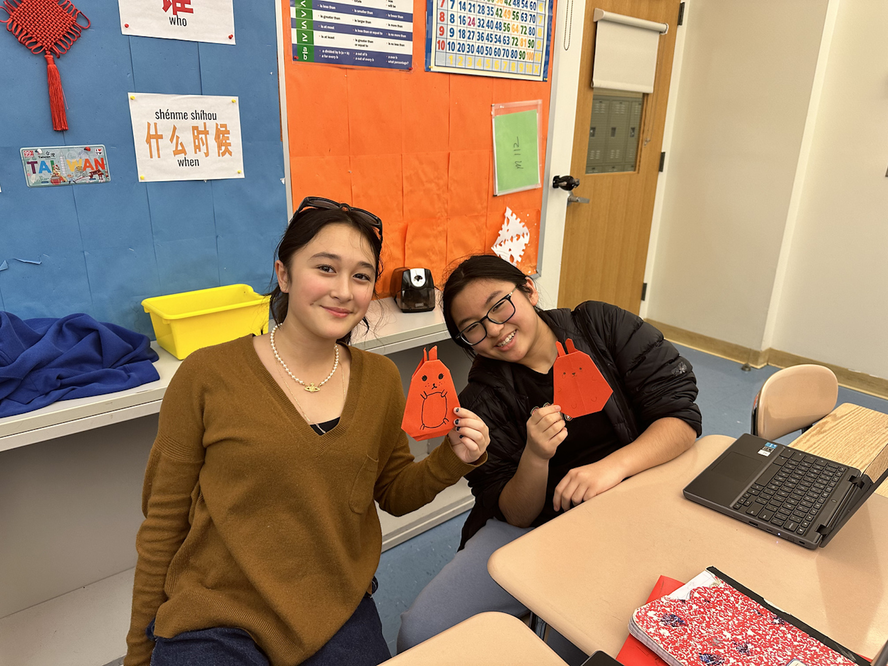 Two Fieldston Middle students smile and hold up their rabbit origami creations.