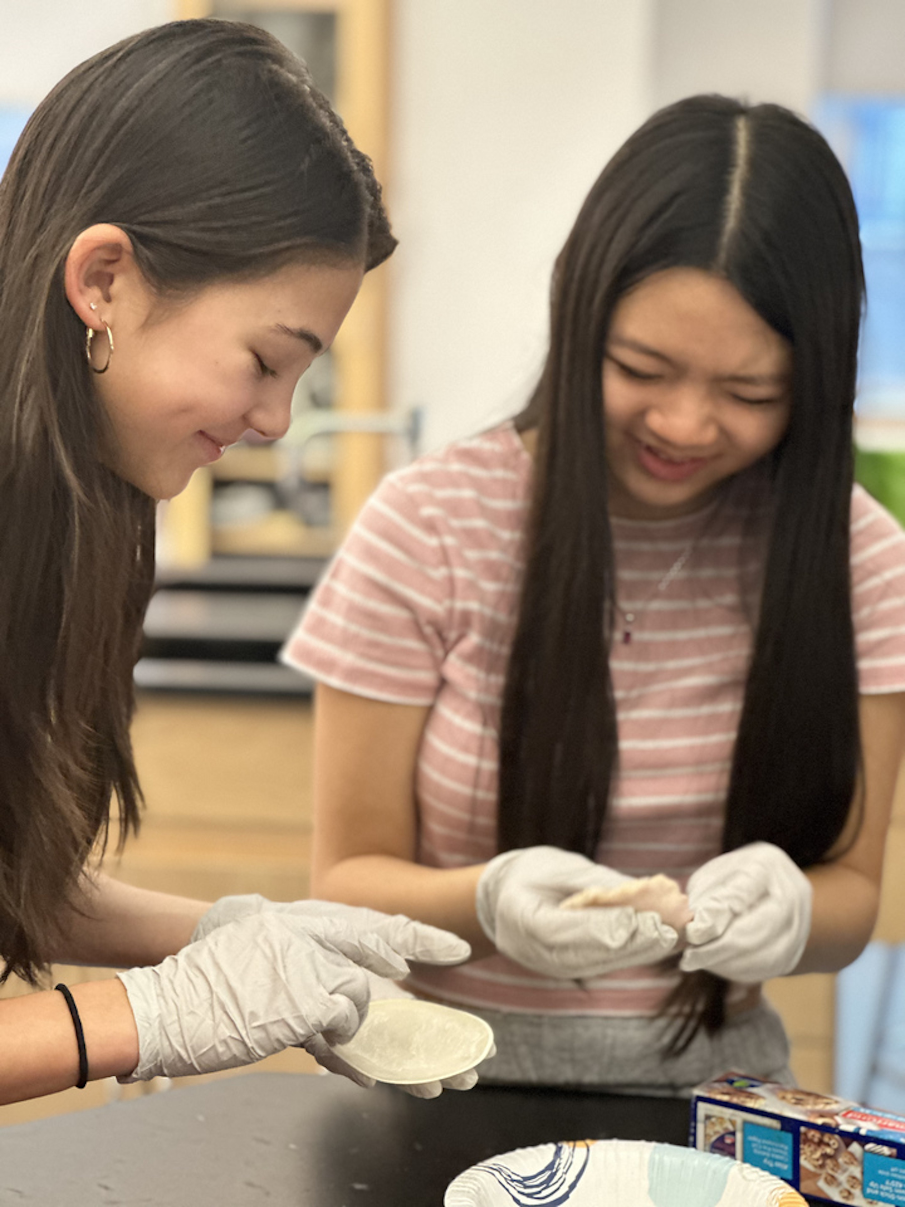 Two Fieldston Middle students wrap dumplings and smile together.