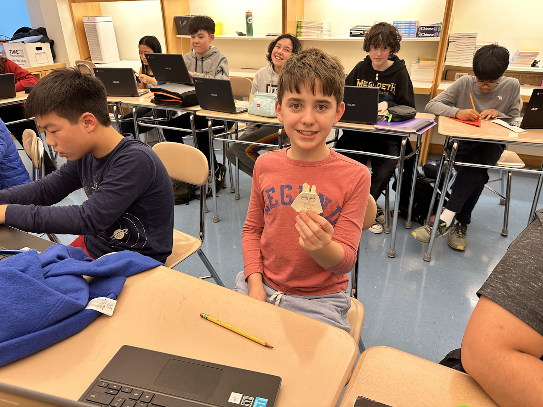 Fieldston Middle student holds up rabbit origami and smiles at the camera.