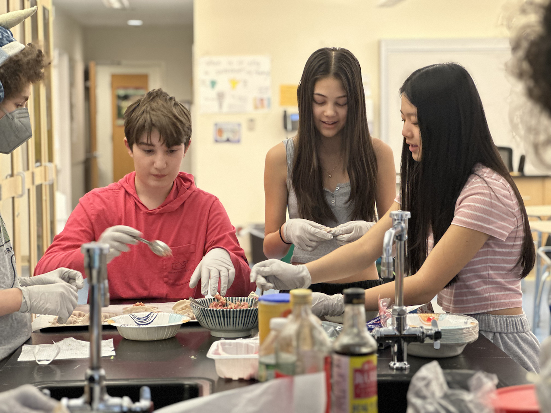 Three Fieldston Middle students work to fill dumplings.