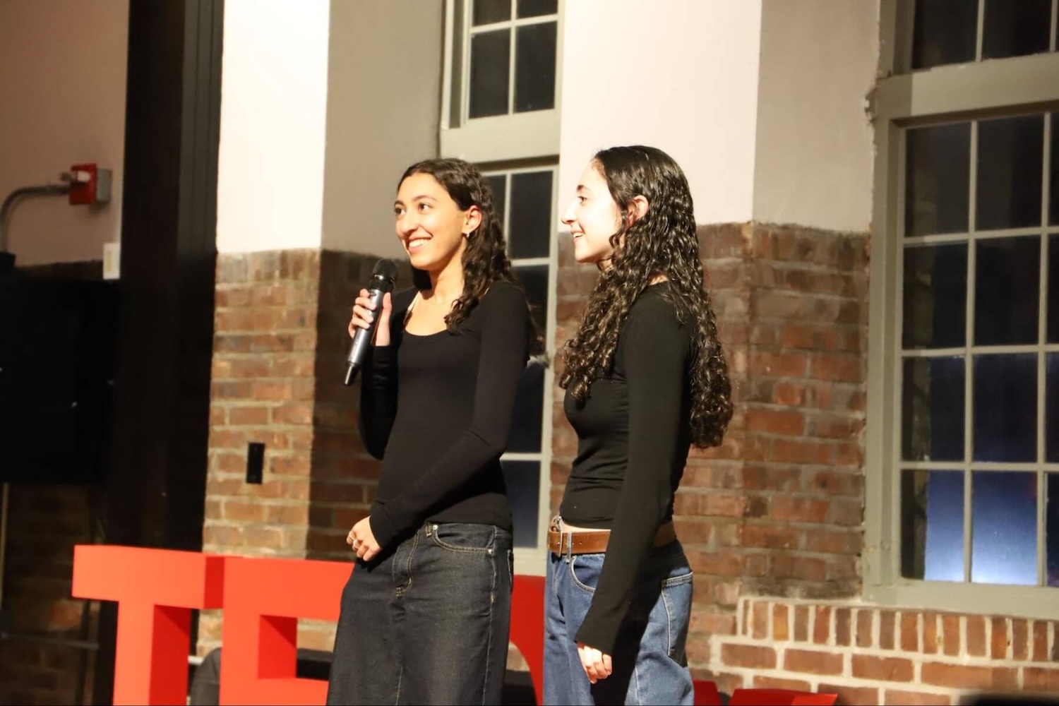 Two Upper School students at Ethical Culture Fieldston School smile and share a mic as they introduce the TEDxECFS event.