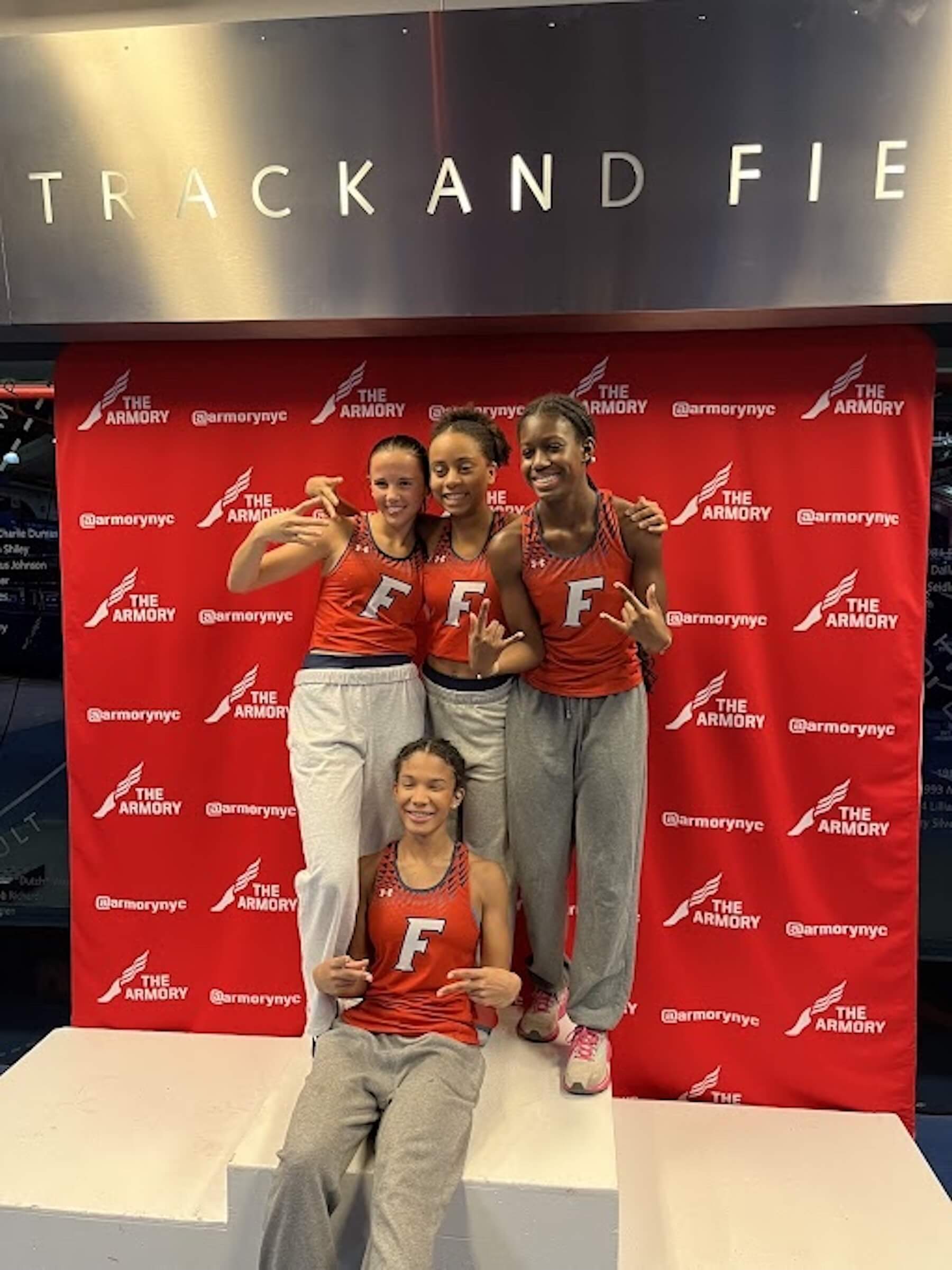 Four Ethical Culture FIeldston School Fieldston Upper Students celebrate on podium after winning at Melrose games track meet