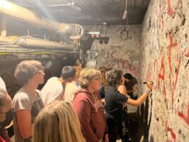 Students write on concrete wall in underground tunnel.