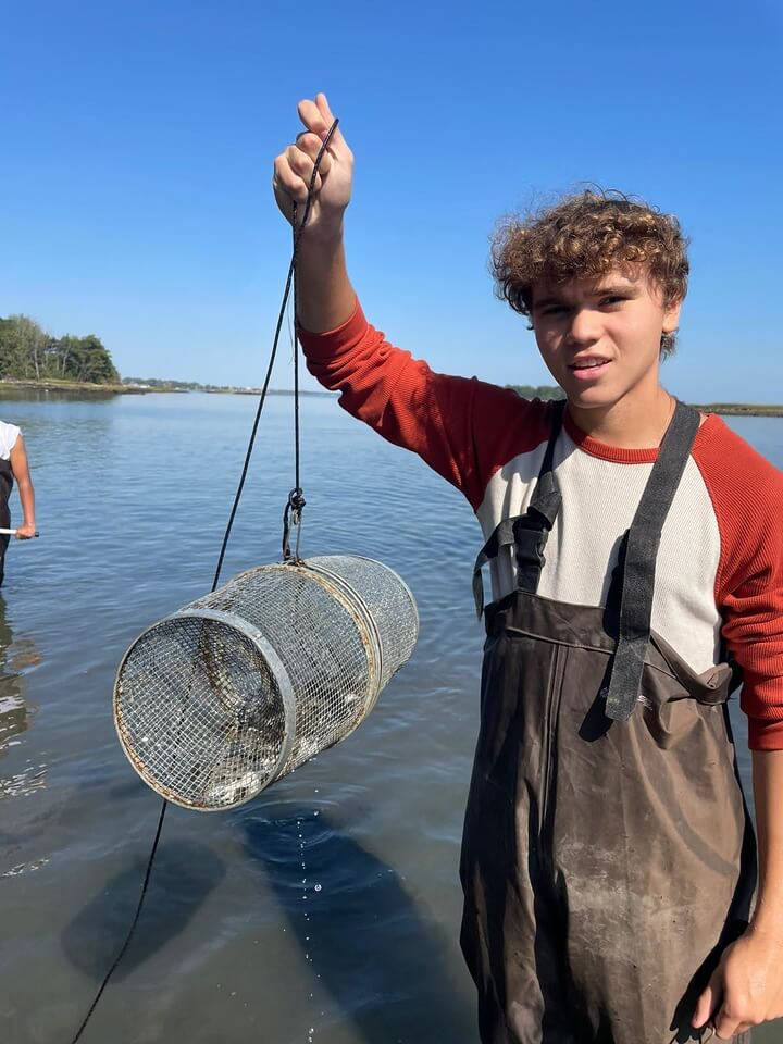 Student wades in water while holding up a fishing net.