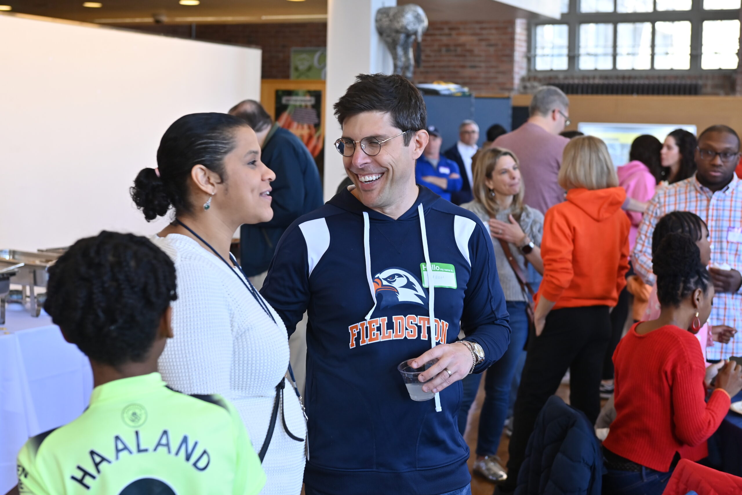 A candid picture of two adults talking and smiling amidst a larger group of people