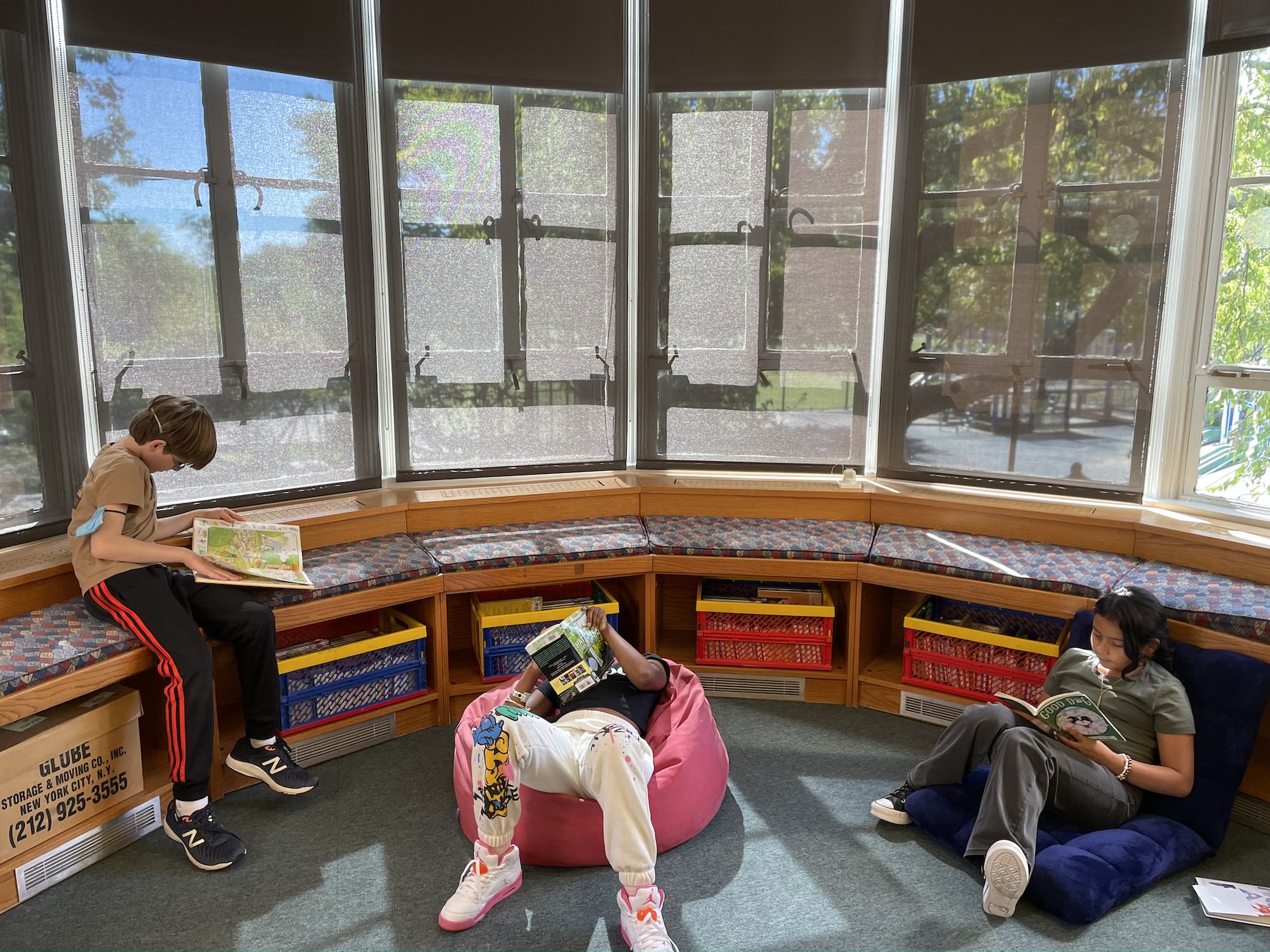 Three students sit and read in front of the windows of Fieldston Lower library