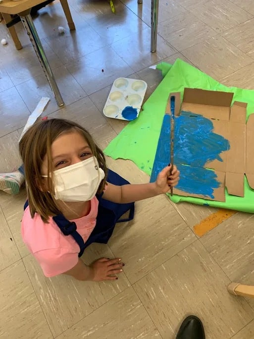 Student holds paint brush and smiles at camera