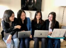 Four members of Females in Finance Club sit around computer smiling
