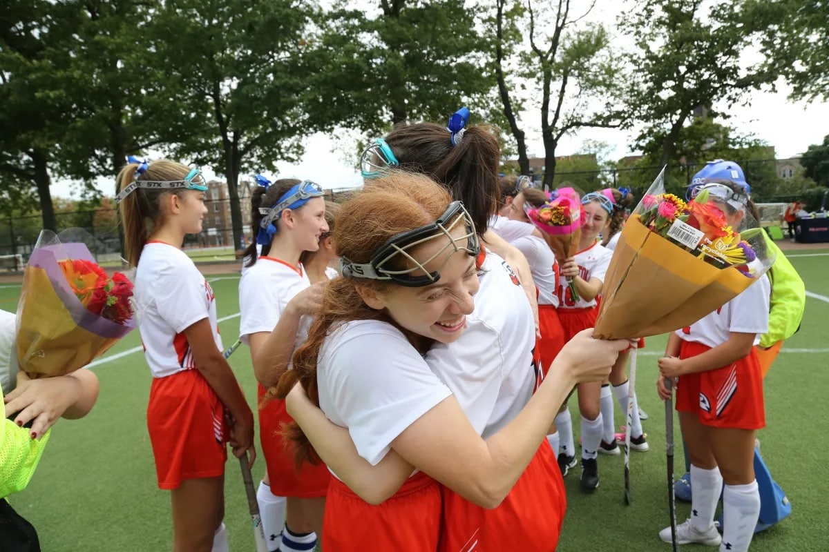 Field hockey players embrace with flowers at homecoming