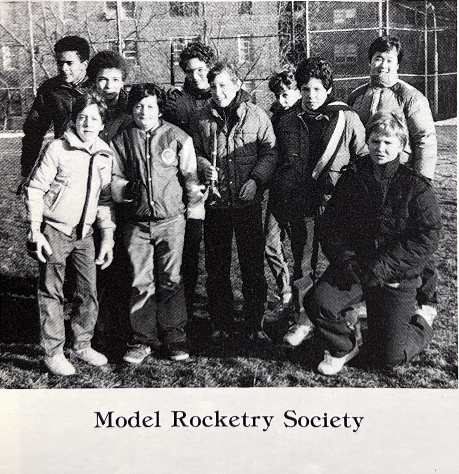 A scanned black-and-white photo from a yearbook shows a group of students posting together, with one student holding a small model rocket. Under the photo is the caption 