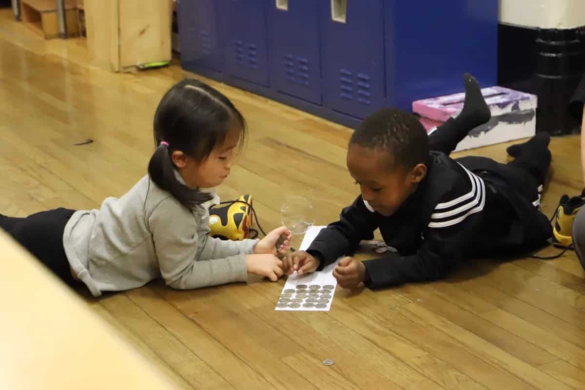 Students count money using paper chart on floor