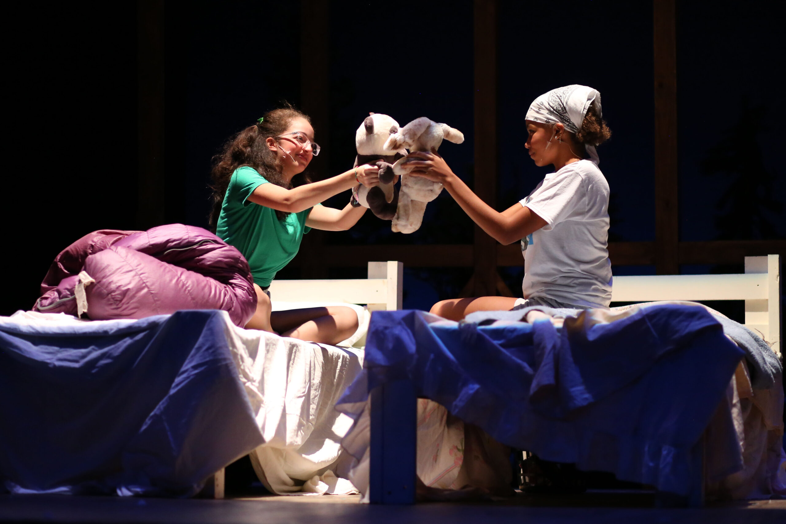 Fieldston Upper students sitting on beds, holding up stuffed animals, while on stage during the fall drama theatre production at the Ethical Culture Fieldston School