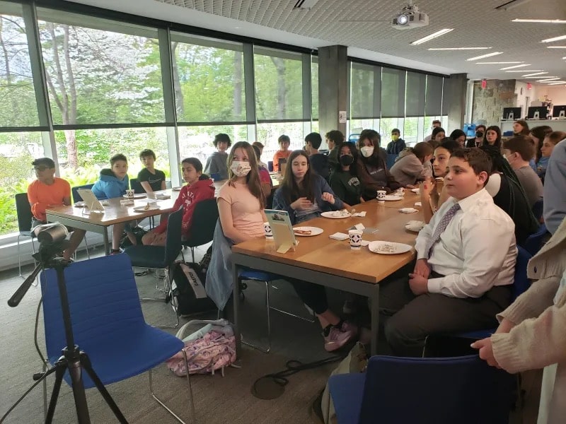 Students listen intently as they sit at a long table indoors